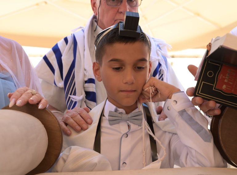 חתן בר מצווה מניח תפילין בטקס עליה לתורה בכותל